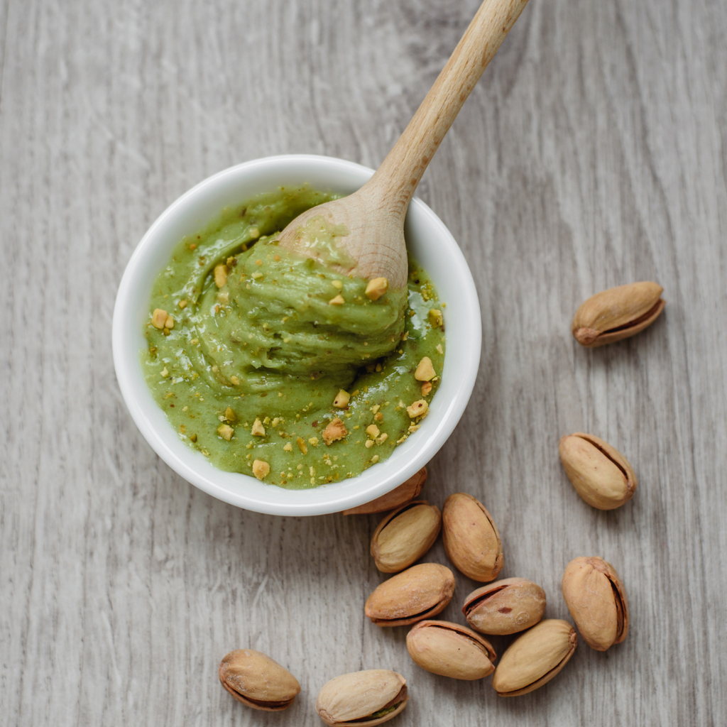 Pistachio paste in a bowl next to loose pistachios, perfect for adding a rich and nutty flavor to your dishes.