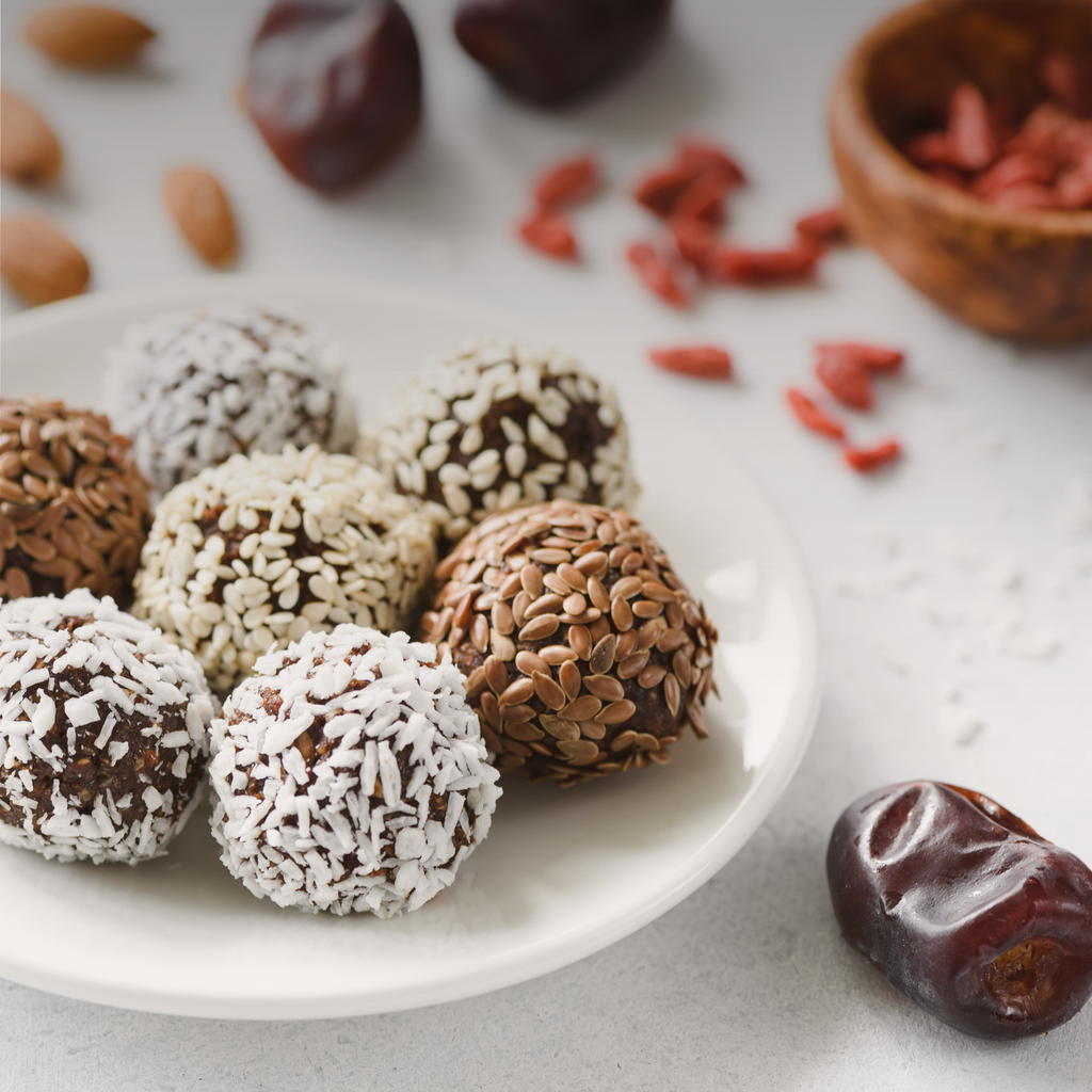 A plate of assorted energy balls with different toppings like coconut flakes, flax seeds, and sesame seeds, next to a single loose date. A perfect snack for those following a caveman diet.