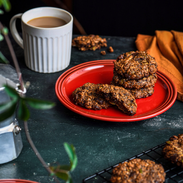 Stack of oatmeal cookies on a red side plate beside a white mug of coffee on a dark marble table