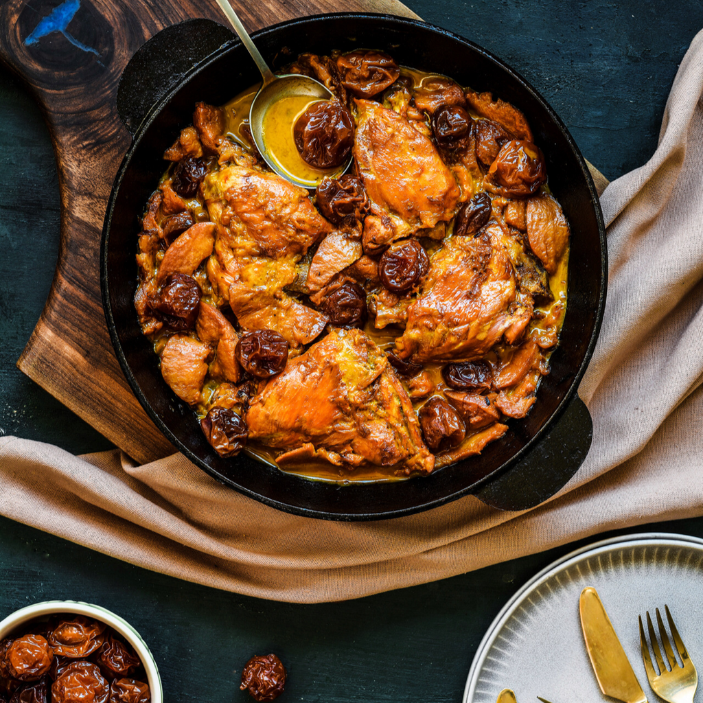 Chicken thighs, plums and quince in a cast iron pan placed on a wooden board on a dark background