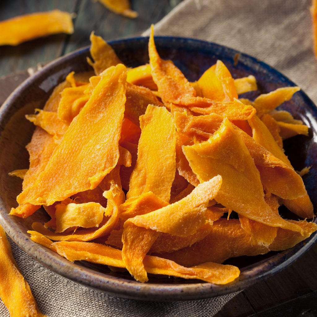 A close-up of a bowl filled with thin, golden-orange slices of dried mango, slightly curled, resting on a brown cloth.