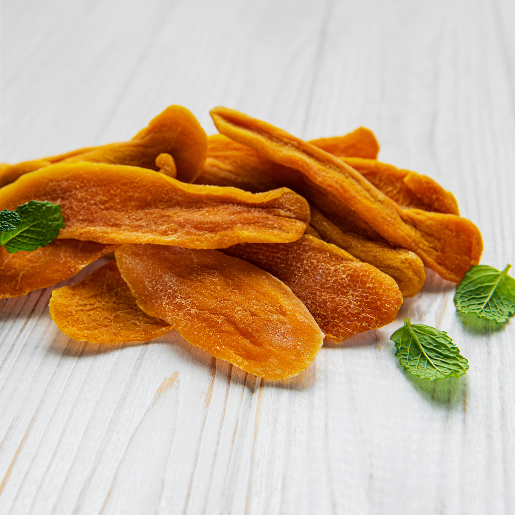 Dried mango slices on a white wooden surface with mint leaves.