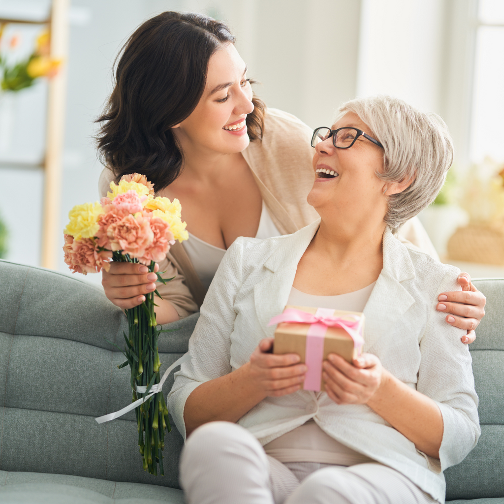 Mother and daughter smiling with flowers at home on Mother's Day.