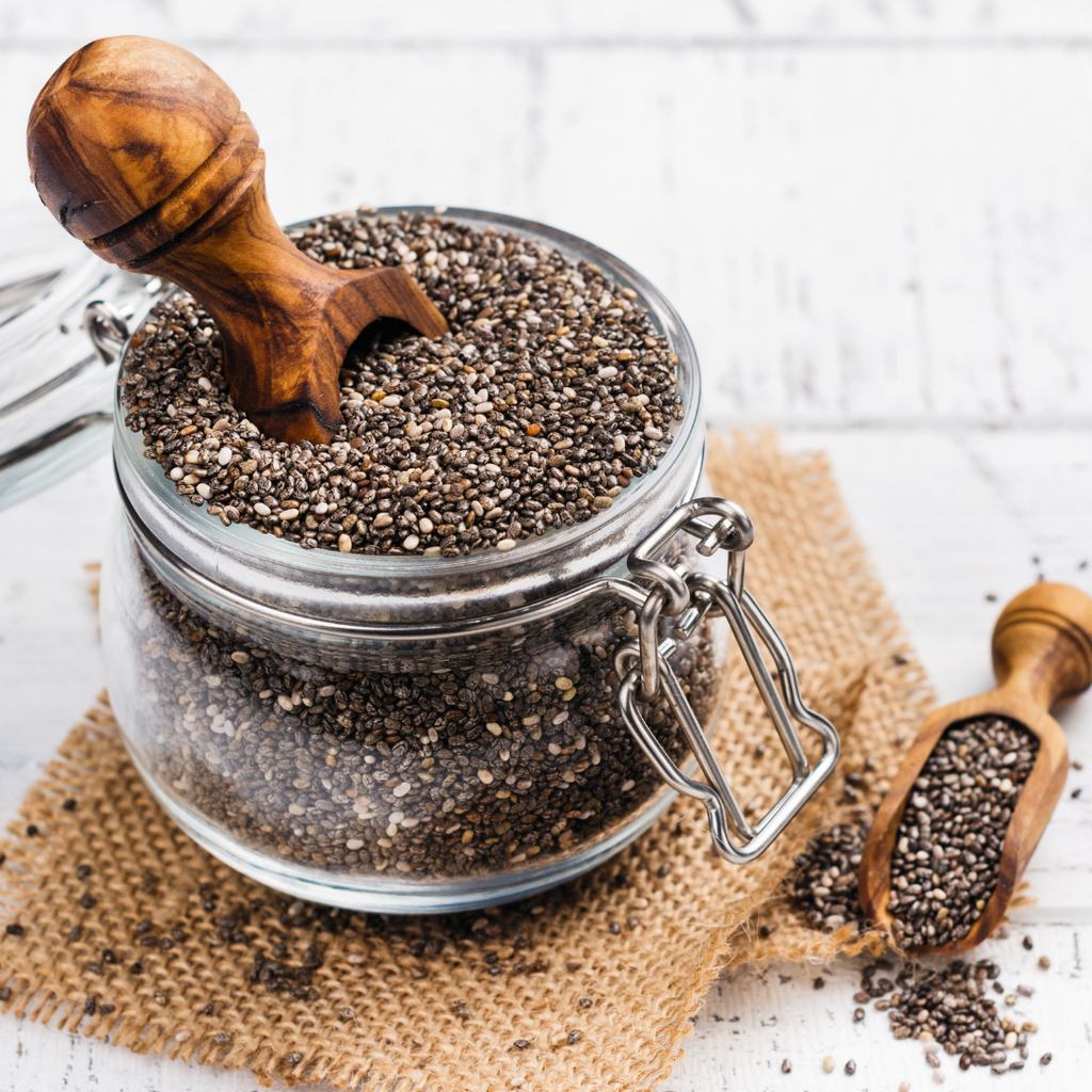glass pot of full of chia seed on top of a wooden coaster with a wooden spoon lodged in it
