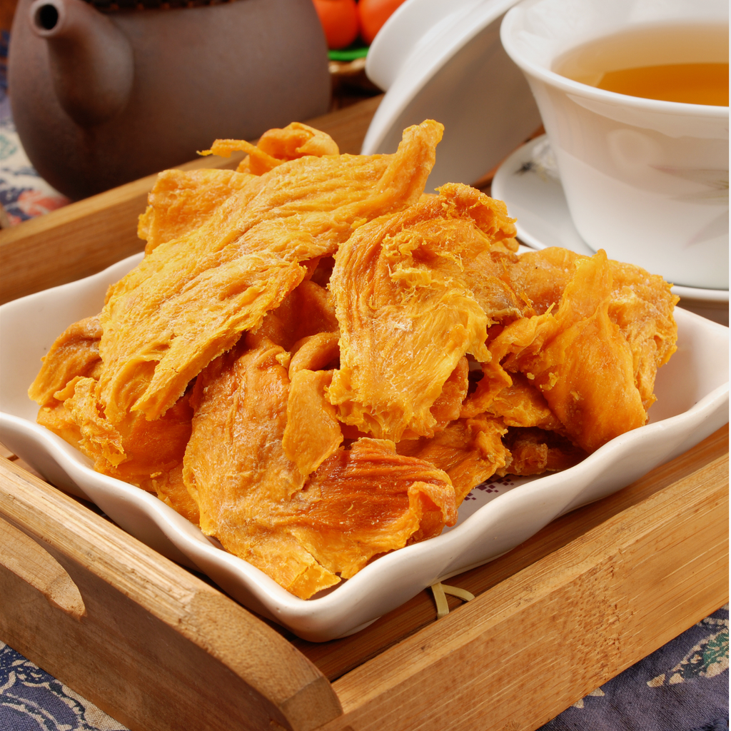 Plate of dried mango pieces beside a cup of tea.
