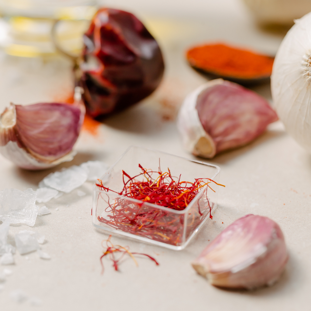 A small square box containing red saffron, a vibrant spice known for its distinct flavor and color, laid net to garlic on a marble table.