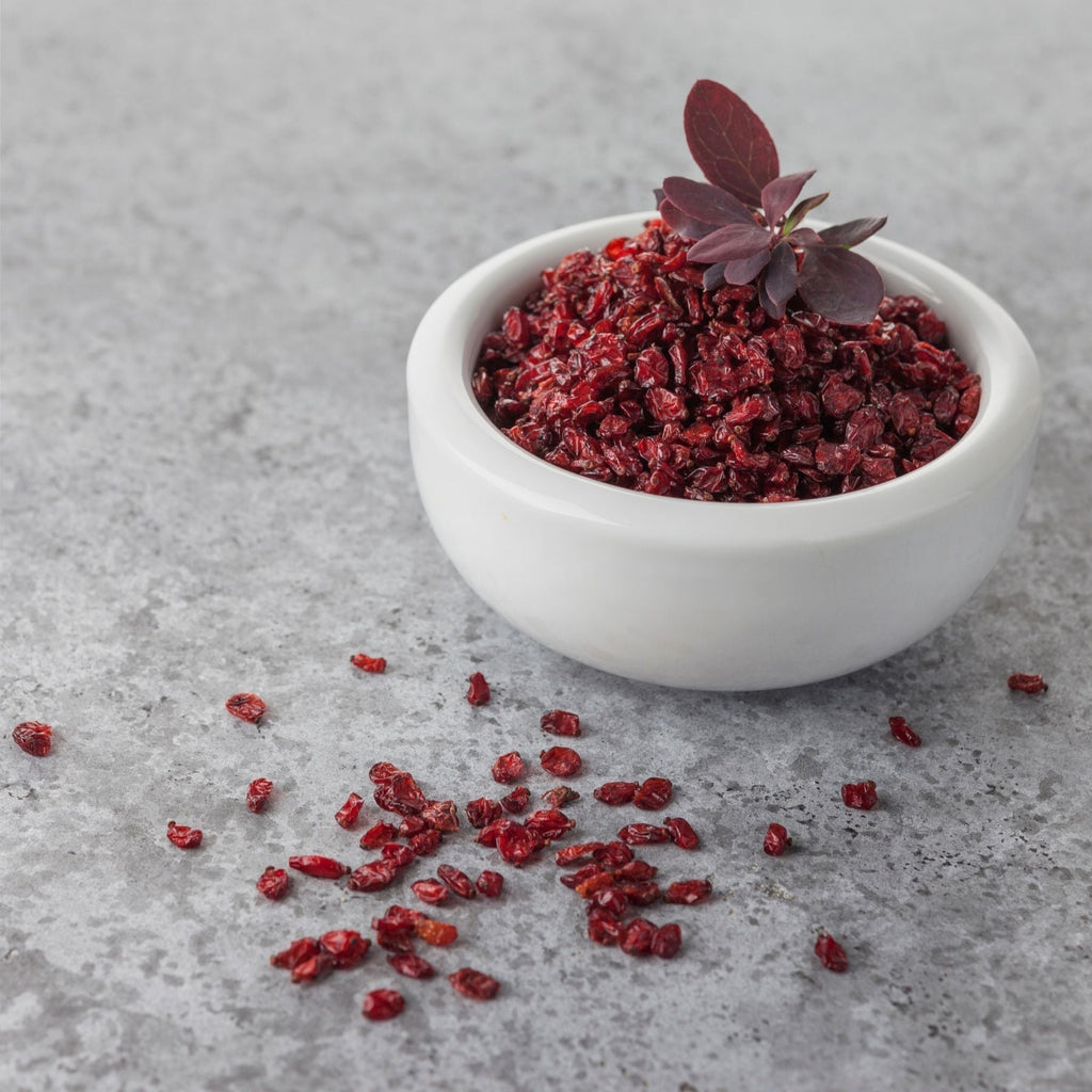 Small white bowl filled with dried barberries, topped with a purple leaf sprig.
