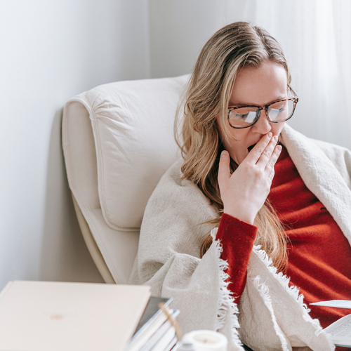 Woman yawning covered in a blanket on an armchair, suffering from extreme fatigue in perimenopause