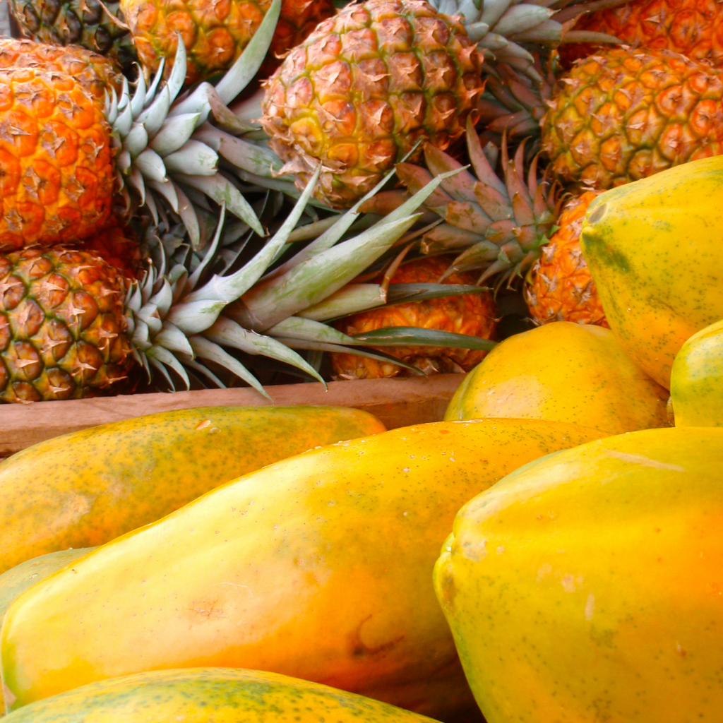 Close-up of fresh pineapples and ripe yellow papayas piled together.