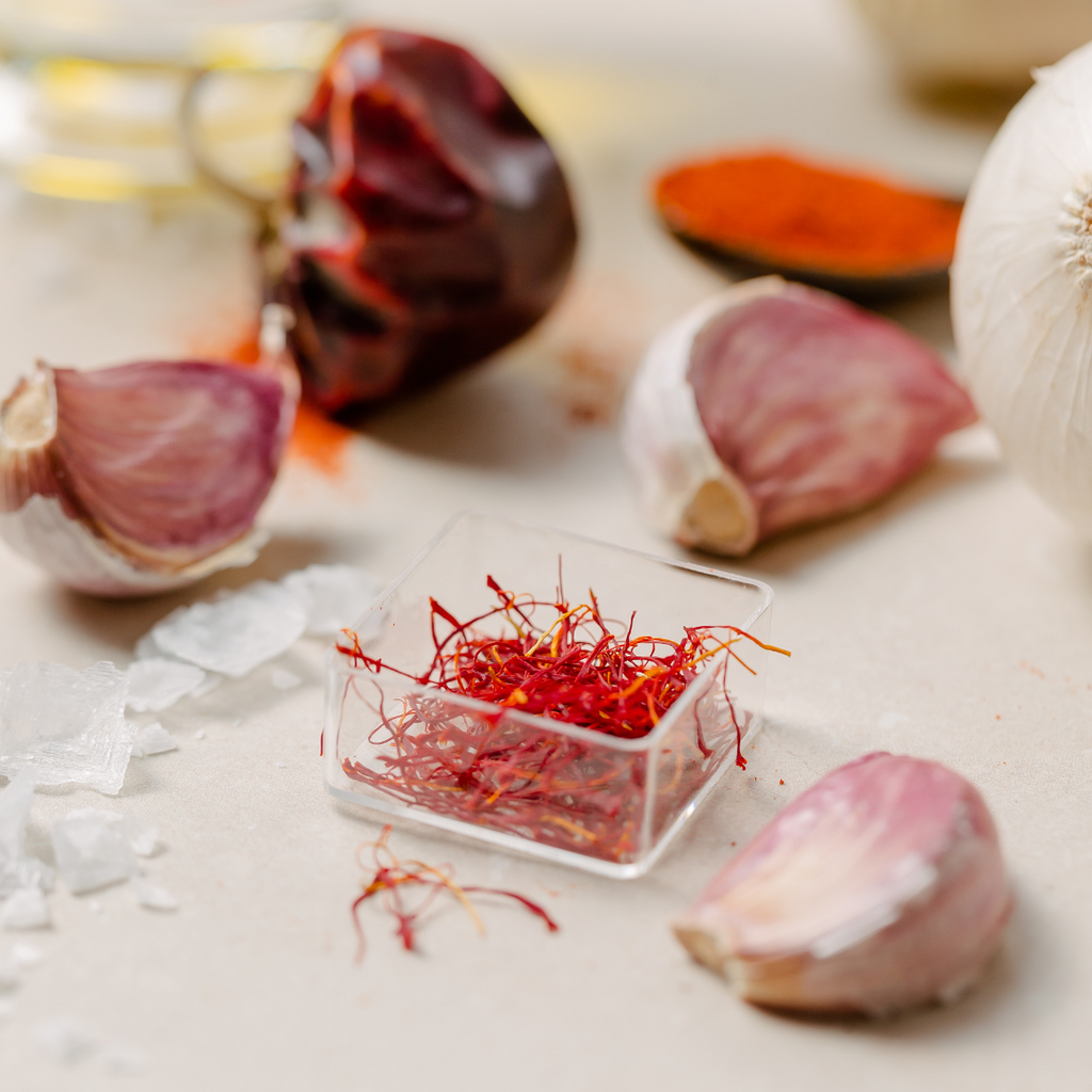 A small plastic jar of saffron threads next to some garlic cloves on a table.