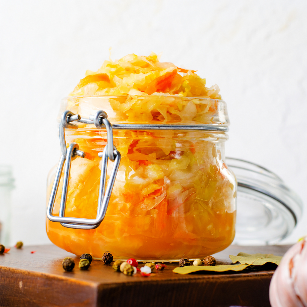 Glass jar filled with vibrant homemade sauerkraut with carrots, surrounded by scattered spices and bay leaves on a wooden surface – ideal for exploring the best time to eat sauerkraut for gut health.